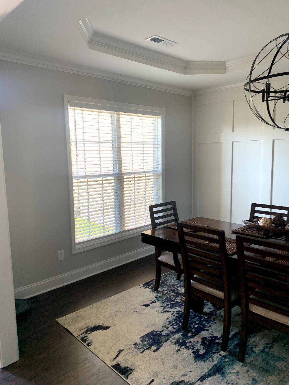 Dining room with dark wood table and chairs, patterned rug, and large window with white shutters.