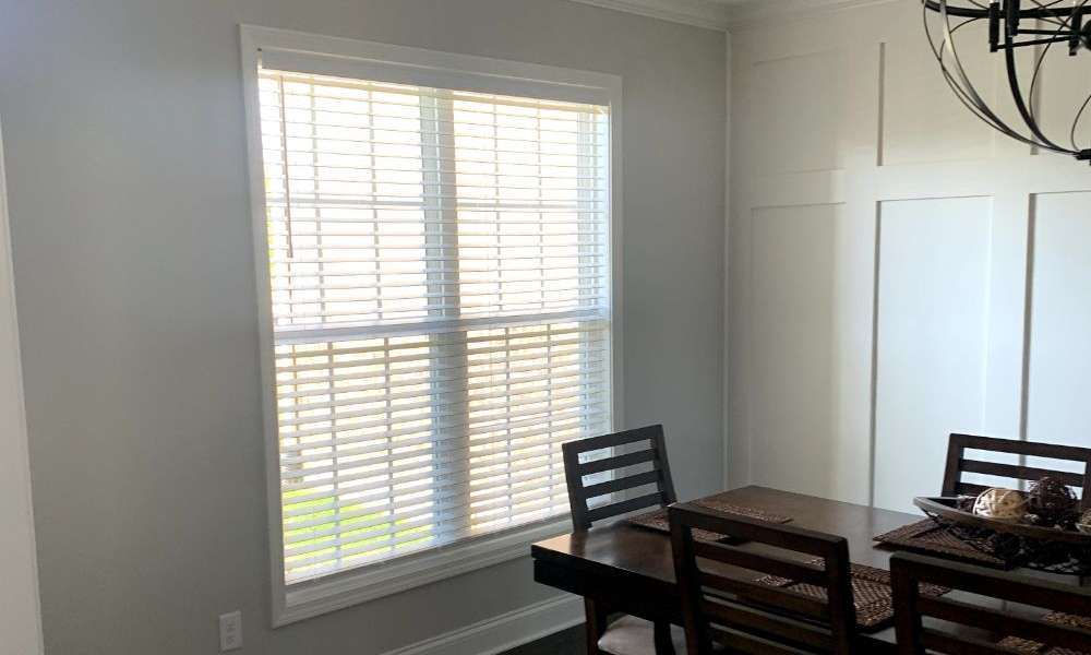 Dining room with a dark wood table and chairs beside a large window with white blinds.