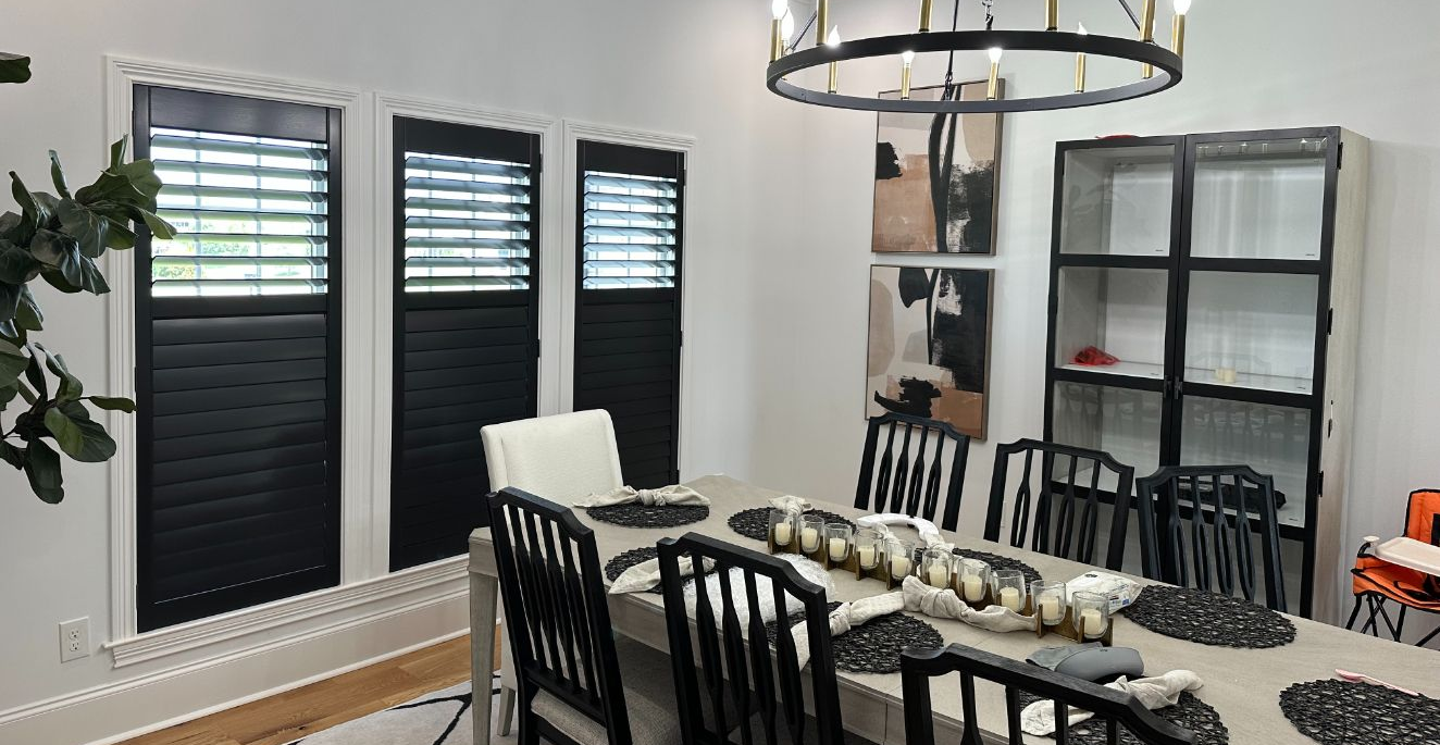 A dining room featuring a wooden table with chairs, black window shutters, a circular chandelier, and a black display unit.