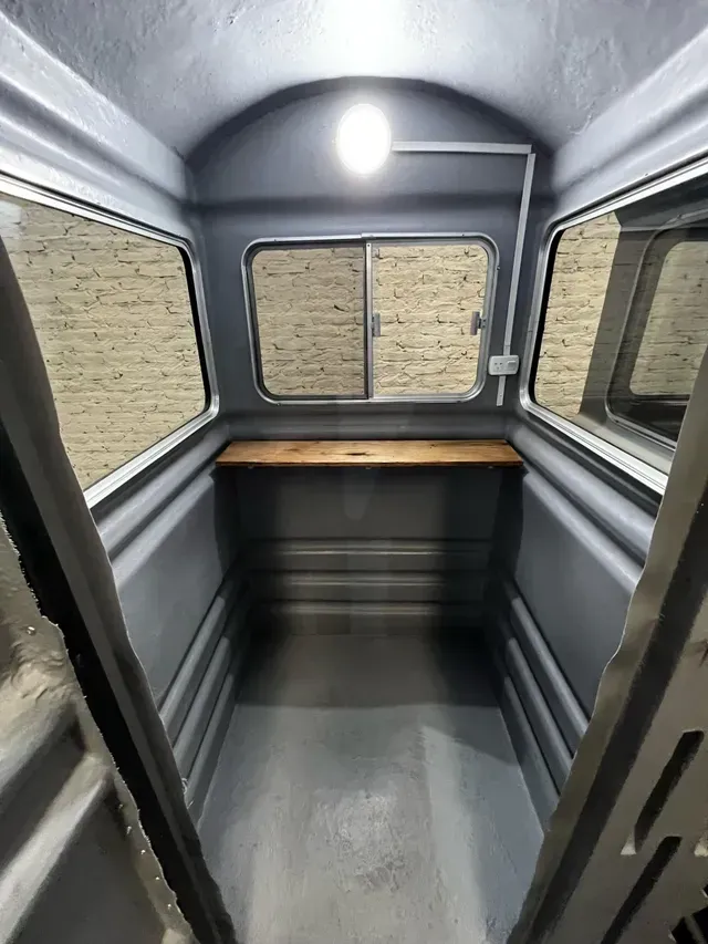 Interior vacío de una furgoneta moderna con paredes grises, suelo negro y una encimera de madera en la parte trasera.