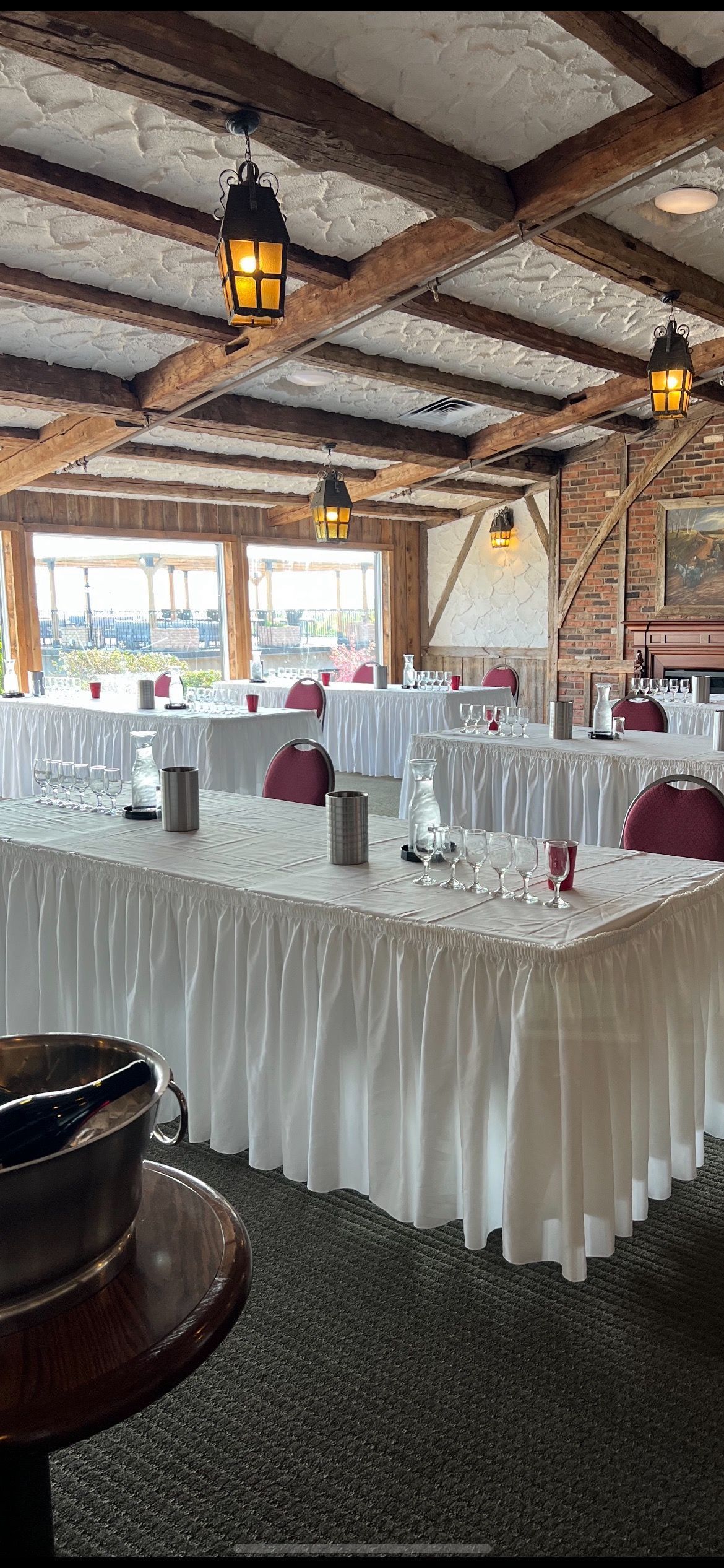 Wedding reception hall with tables set, dark wood beams, and hanging lanterns.