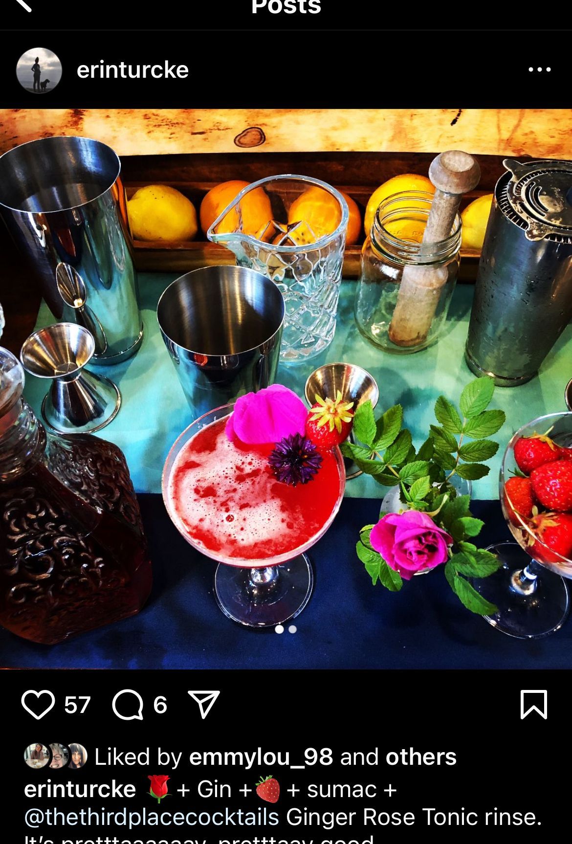 Cocktail setup with a garnished drink, fruit, bar tools, and lemons on a blue surface.