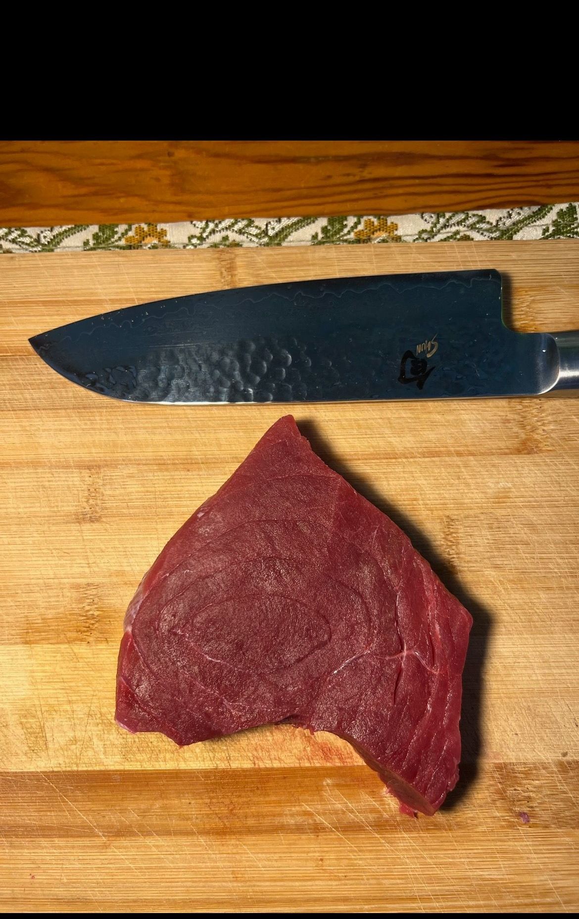 Raw red meat steak and a large knife on a wooden cutting board.