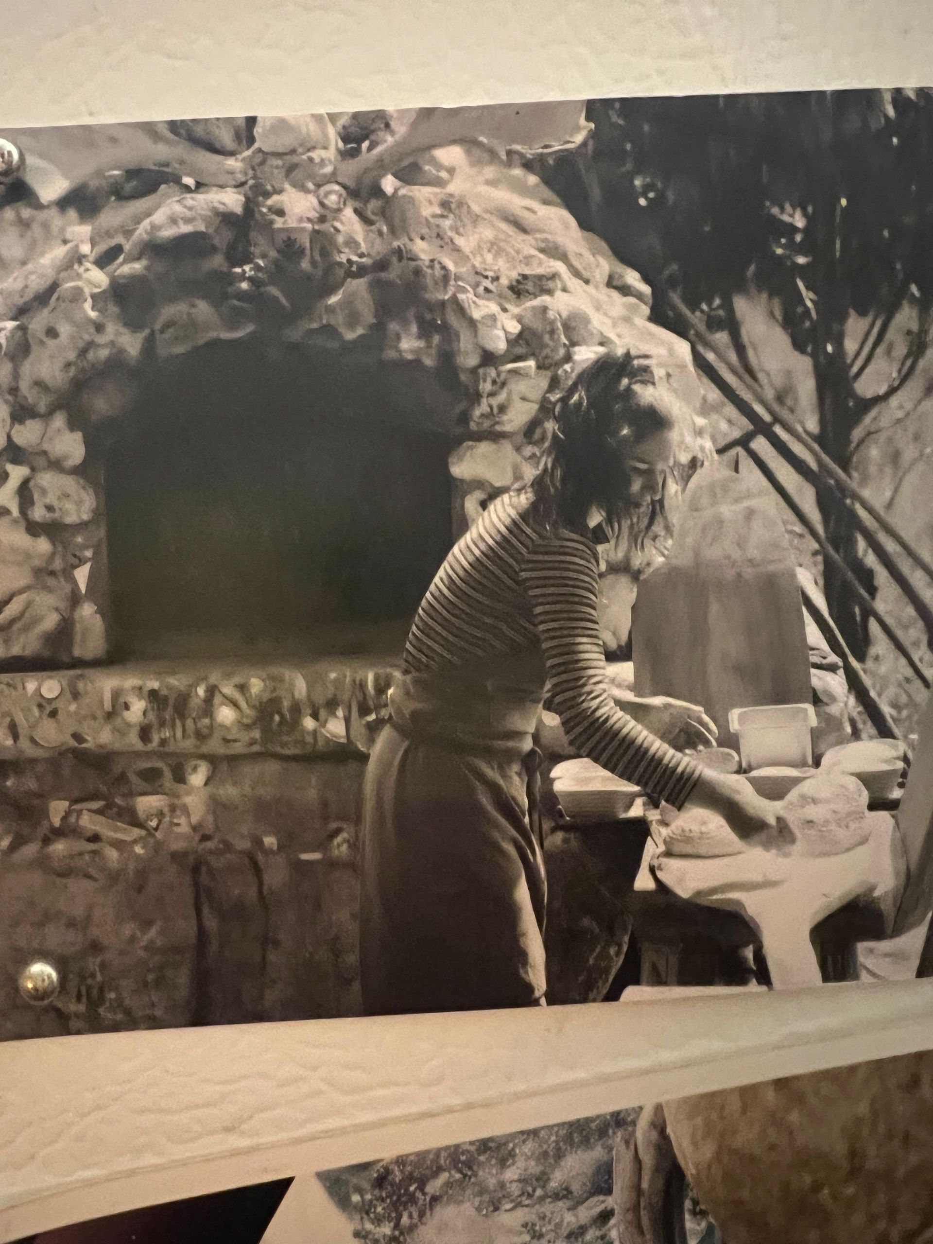 Woman tending stone oven outdoors, working with dough, likely baking.
