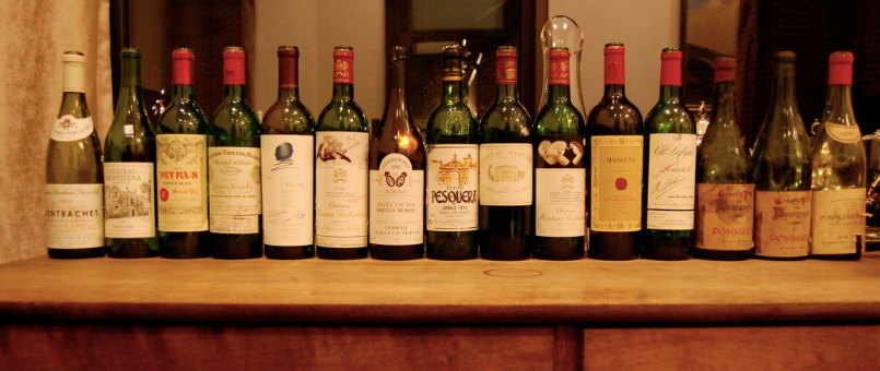 Row of various wine bottles on a wooden surface, with red and white labels, set indoors.
