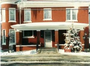 Brick building with snow-covered porch and Christmas tree. Snowy ground in front.