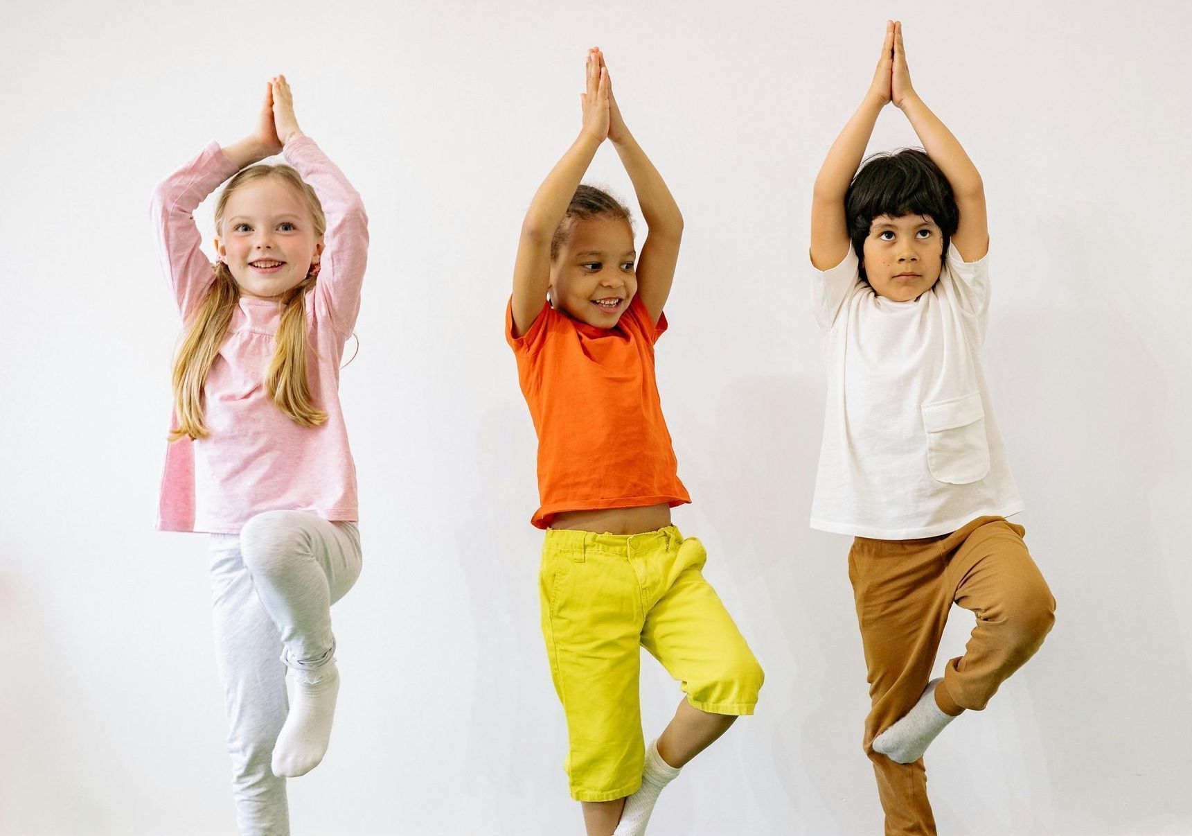 Three children are practicing yoga together.