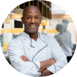 A man in a chef 's uniform is smiling with his arms crossed