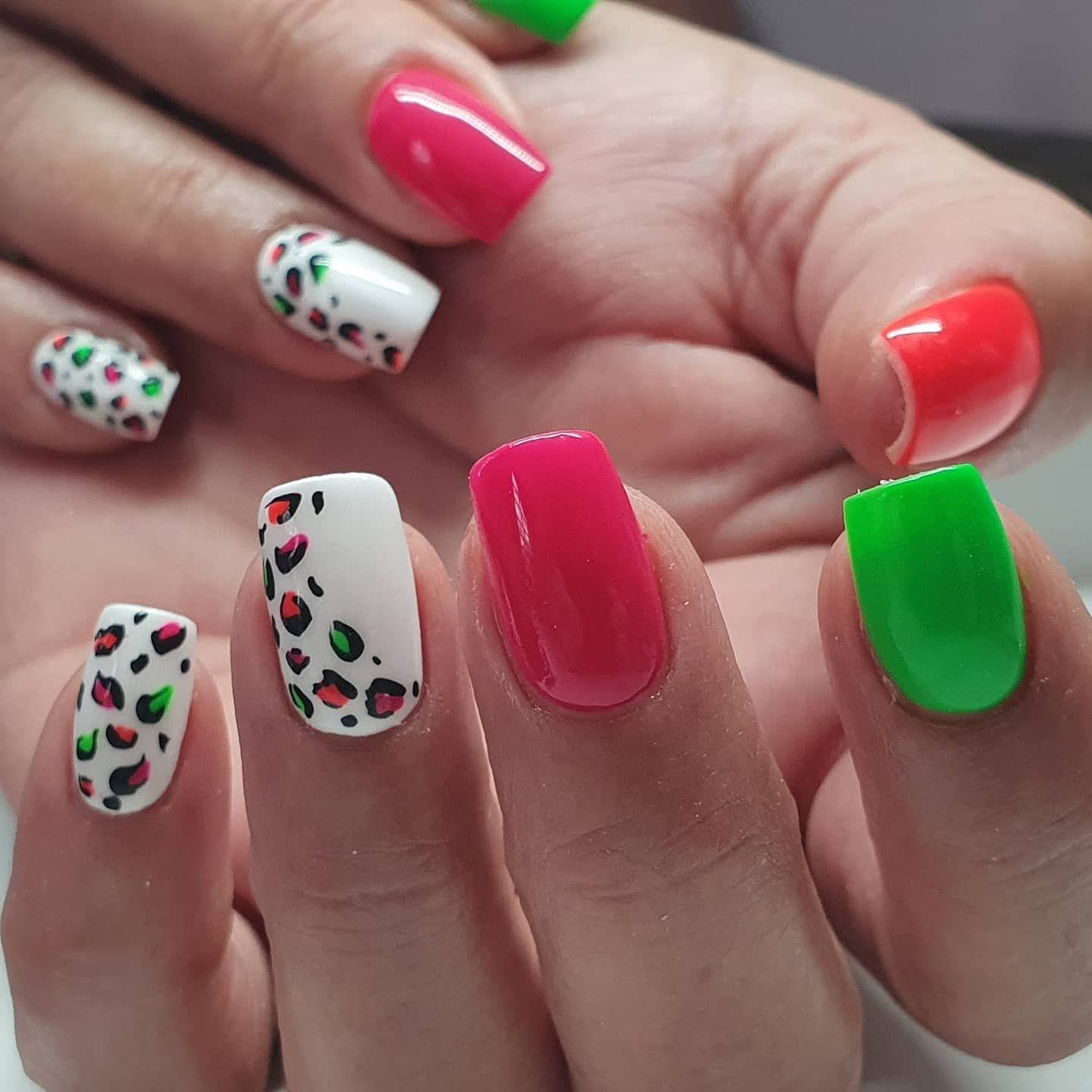 Hand met kleurrijke nail art: roze, groene en witte nagels met cheetahprint.