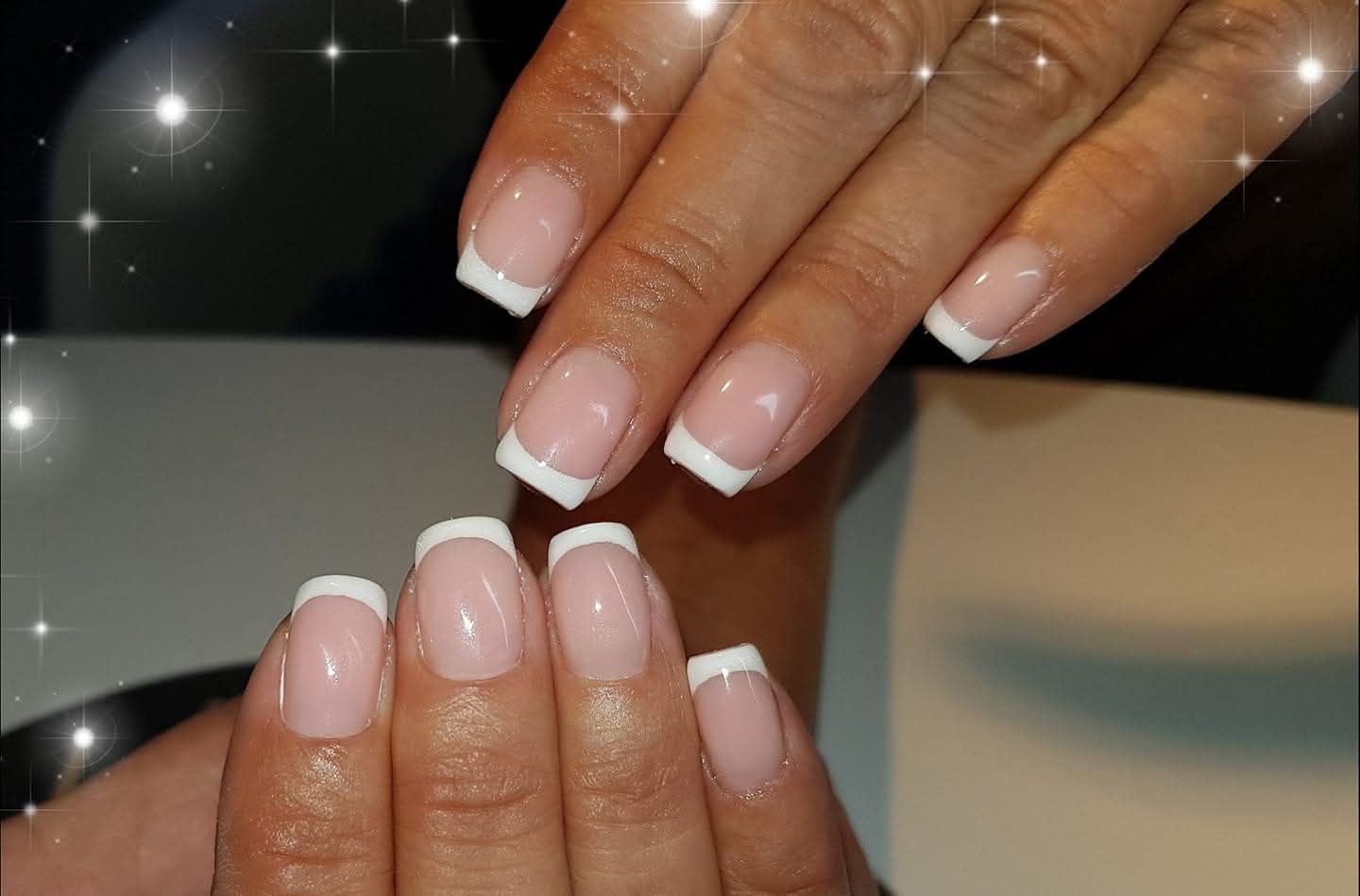 Handen met vierkante nagels in French manicure-stijl; witte nagelpunten, natuurlijke roze nagelbedden.