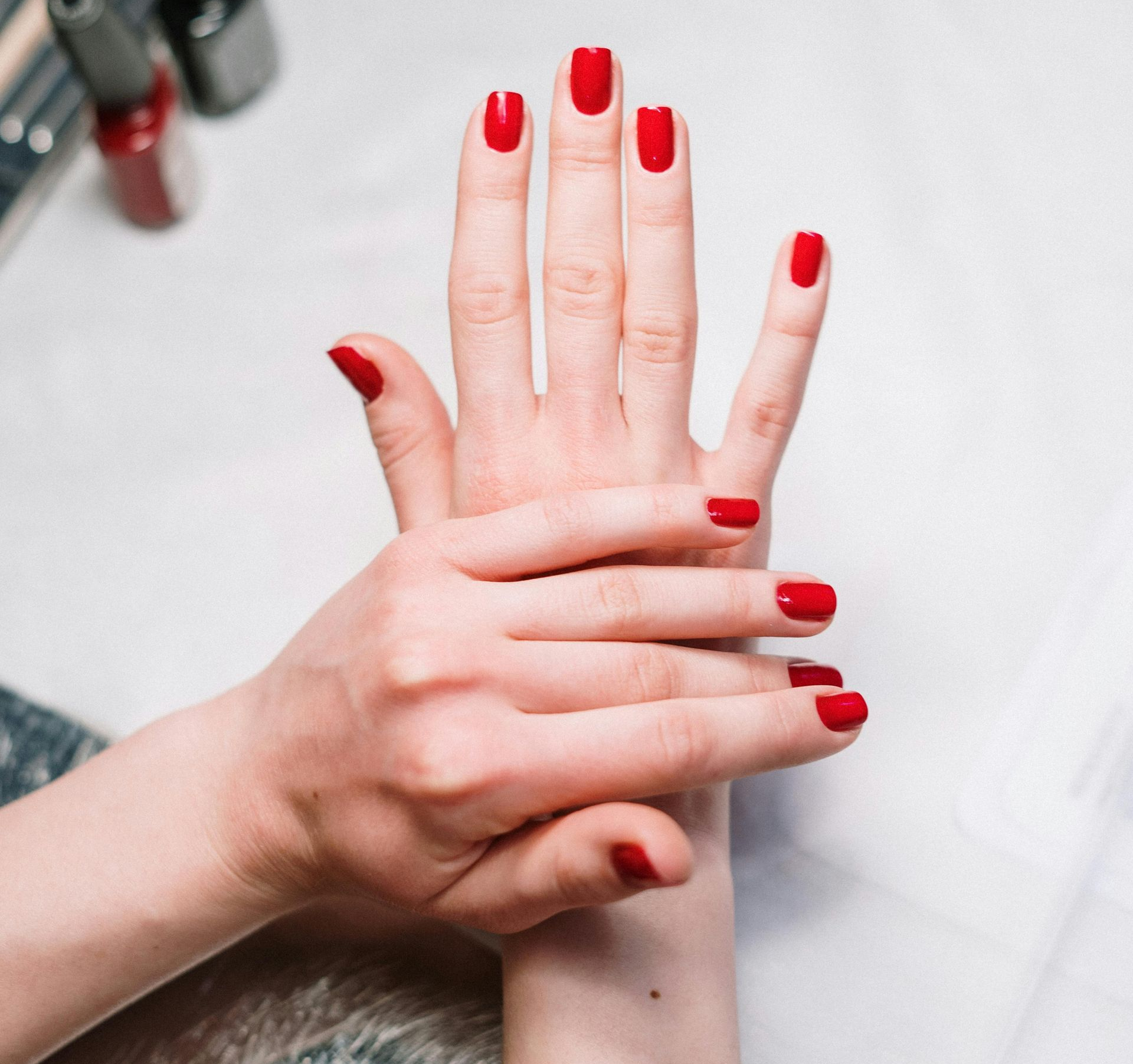 Handen met vers gelakte rode nagels, de ene hand rustend op de andere.