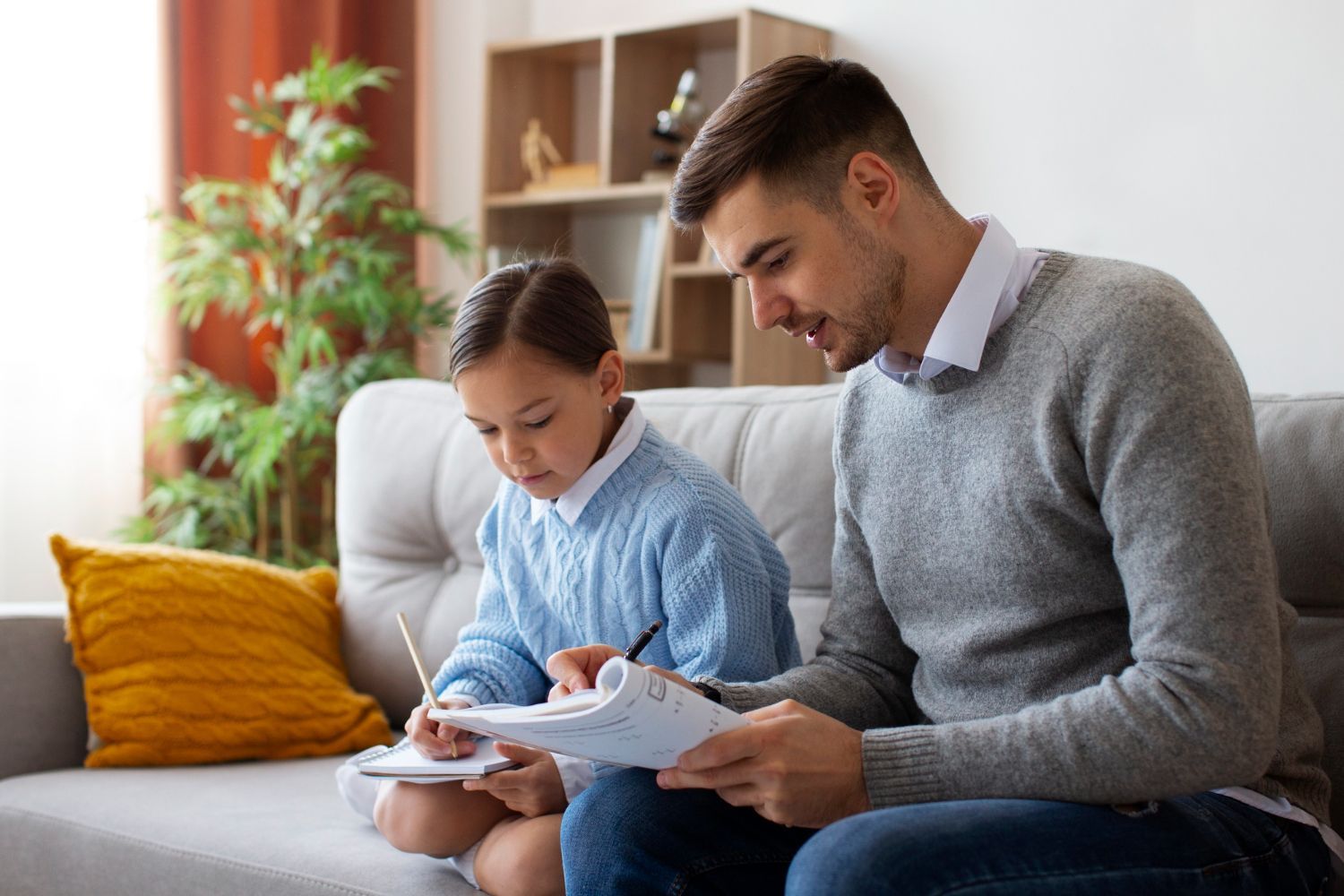 Two people sitting on a couch reading a book together in a bright living room
