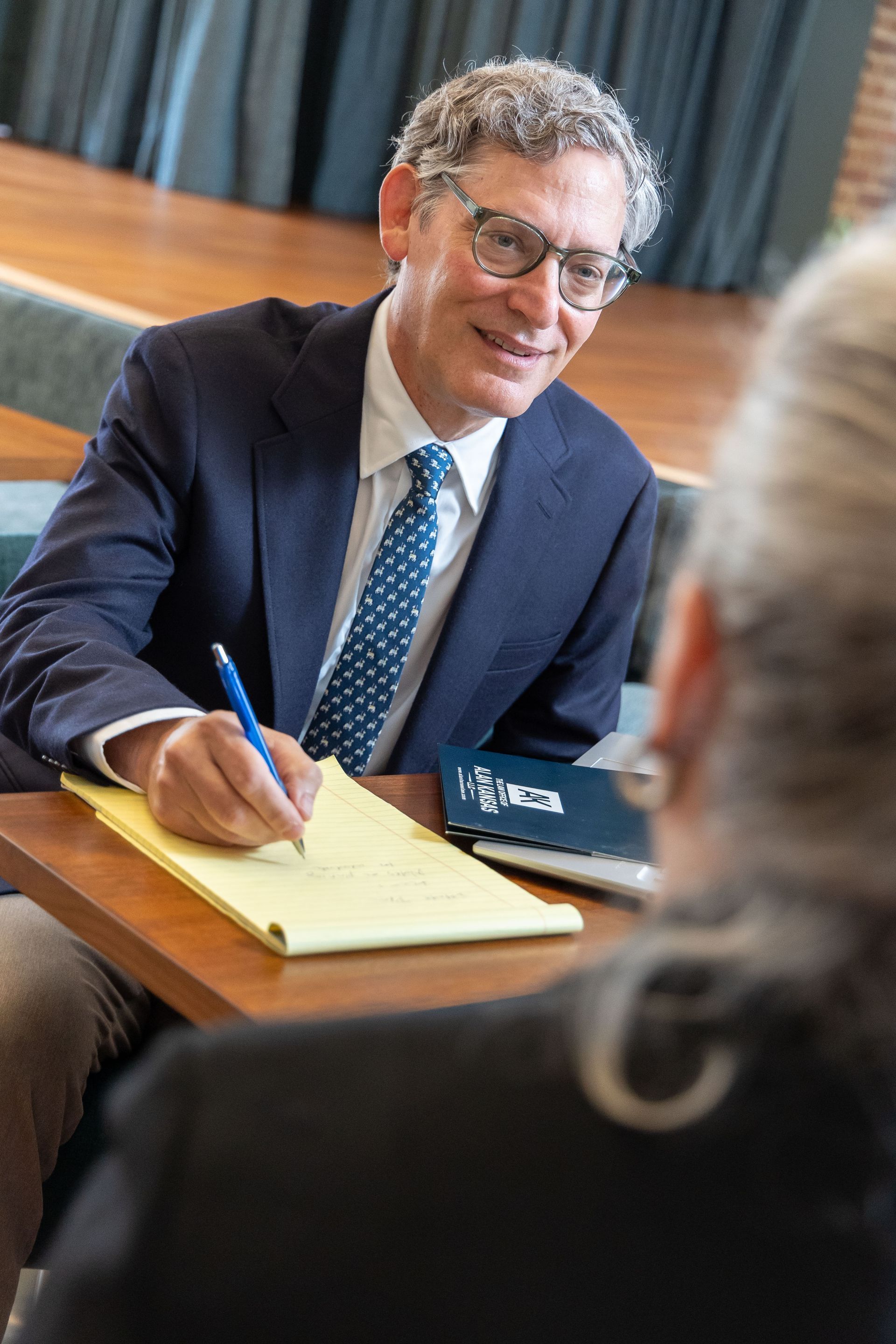 Man in a suit signing papers at a meeting table with a blue pen
