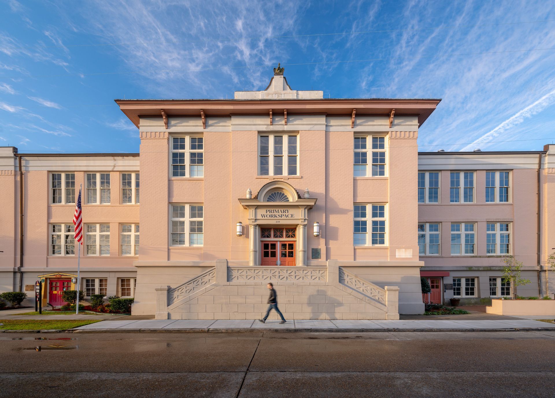 Historic pink civic building with steps, central entrance, and American flags under a blue sky