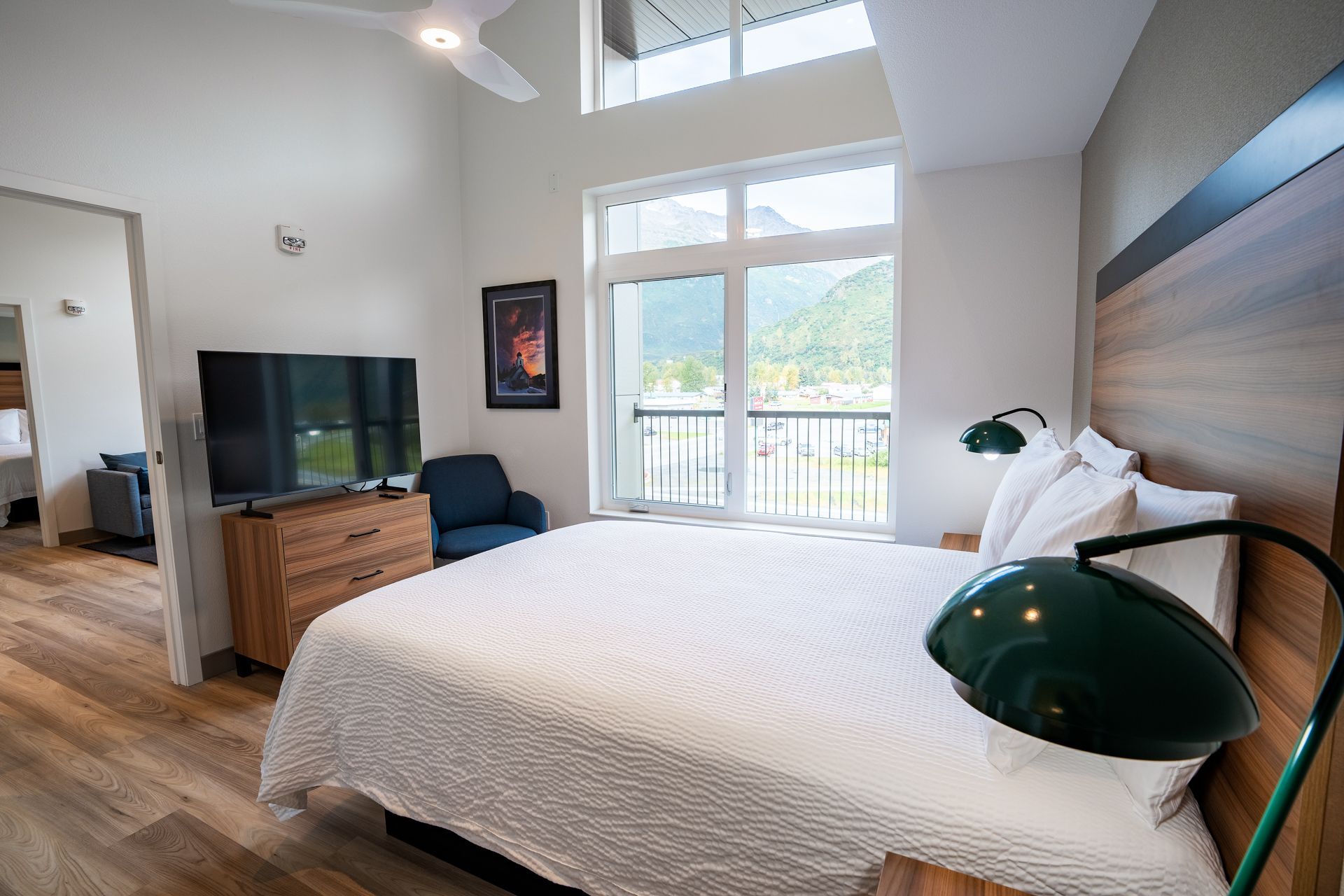 Bedroom with a bed, TV, dresser, chair, and large window overlooking a balcony.