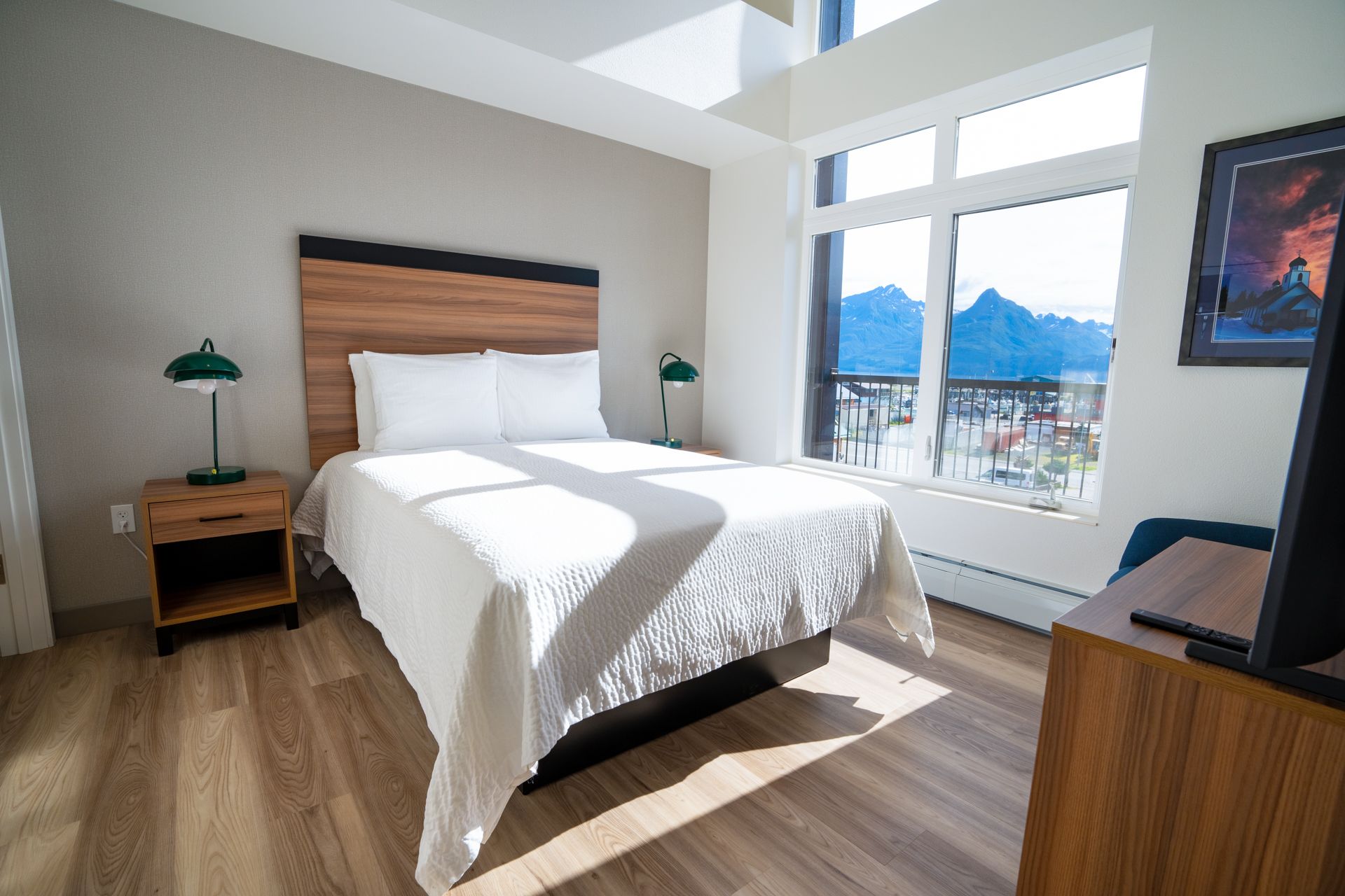 Bedroom with a bed, nightstand, lamps, large window with a mountain view, and wood floors.