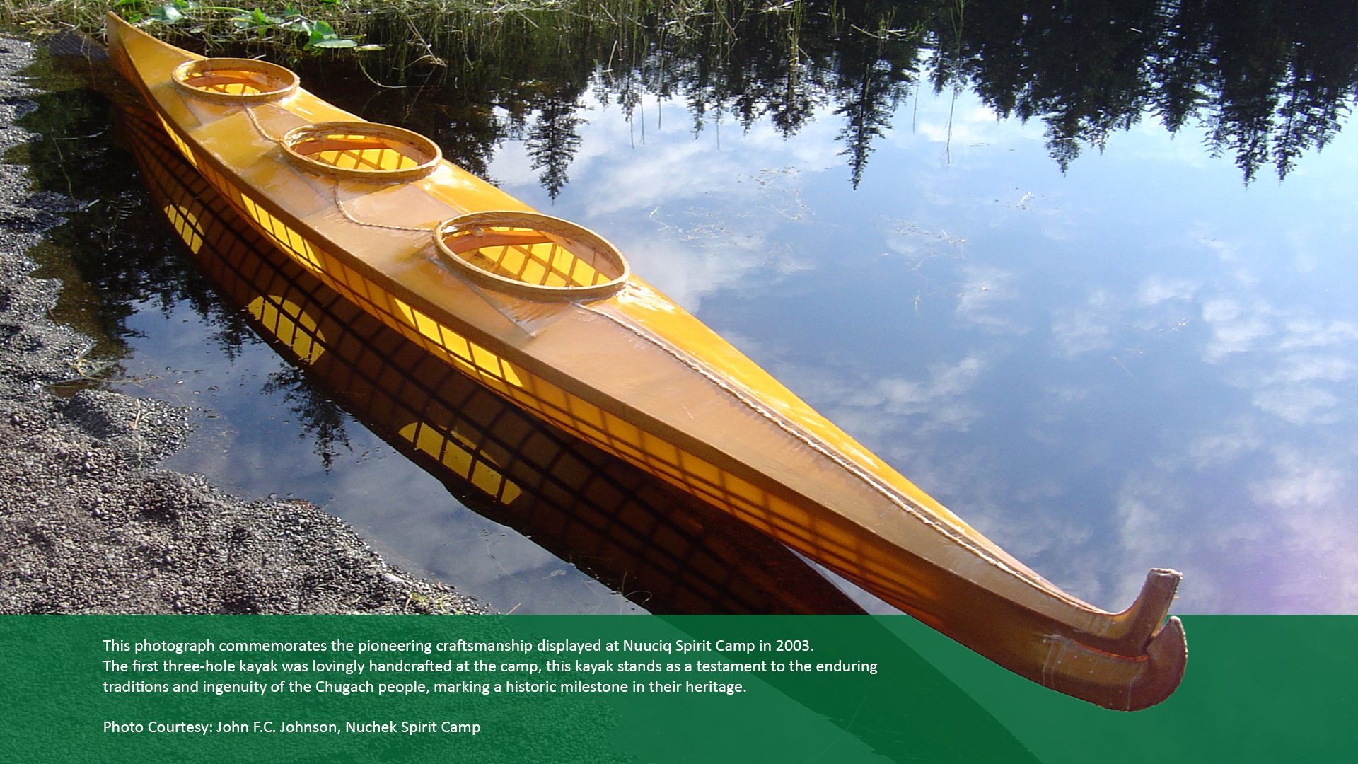 Wooden, three-person kayak on calm water, reflecting trees.
