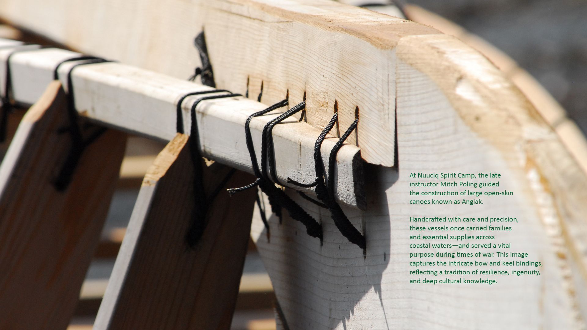 Close-up of wooden boat frame construction, showing lashed support beams and text.