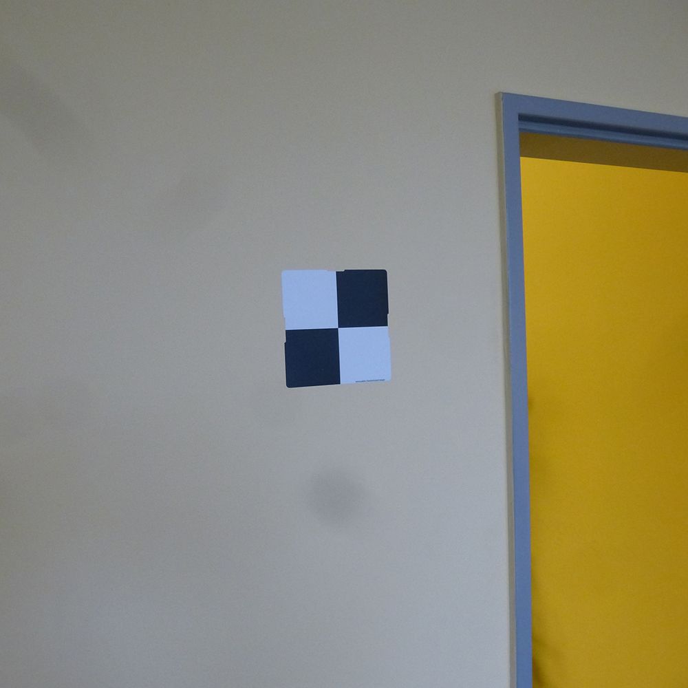 A black and white checkered square is hanging on a wall next to a yellow door.