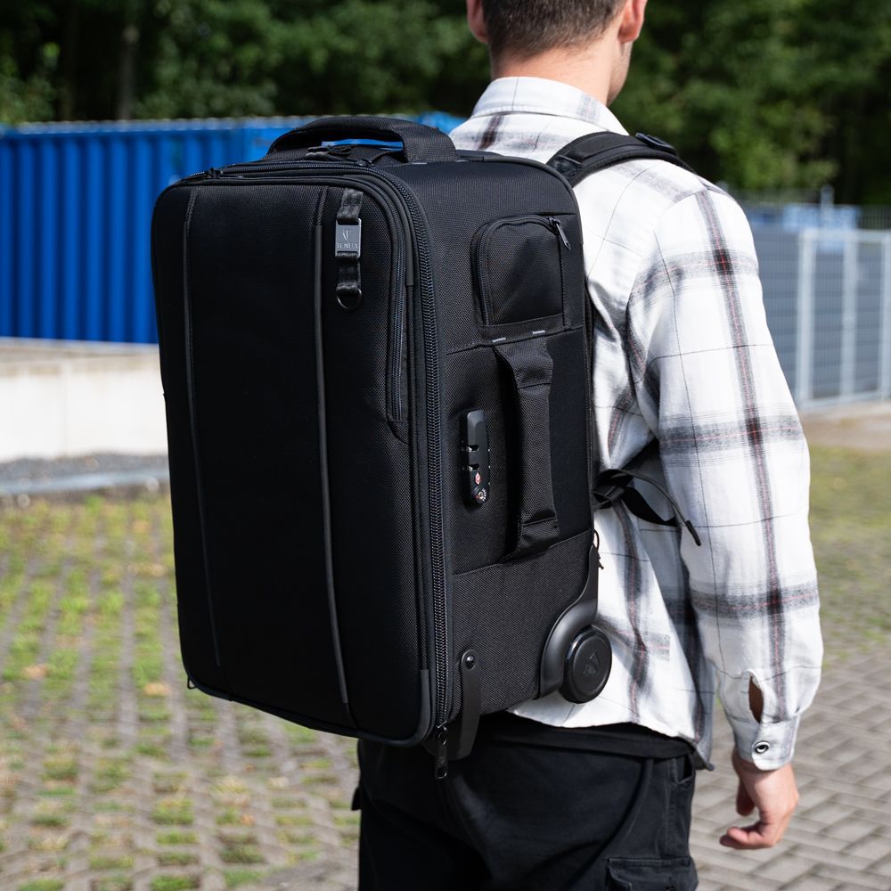 A man in a plaid shirt is carrying a black suitcase on his back