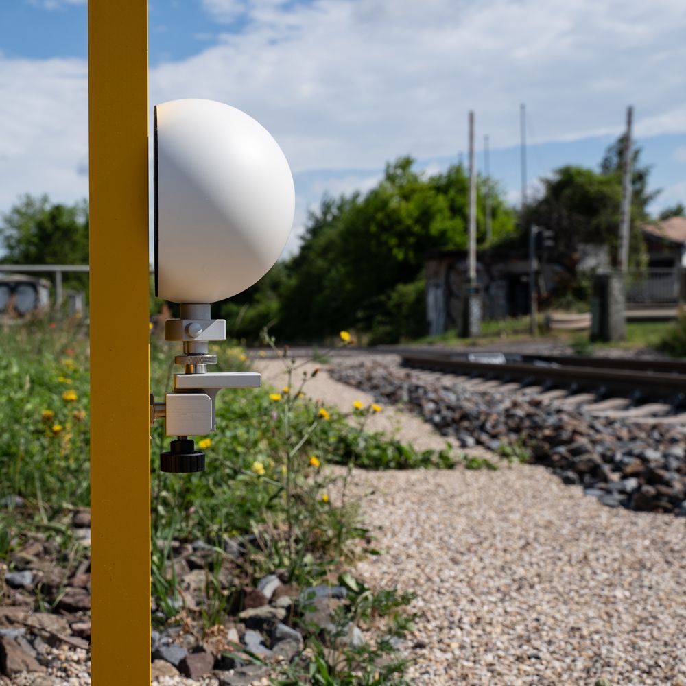 A yellow pole with a white ball attached to it is next to a train track.