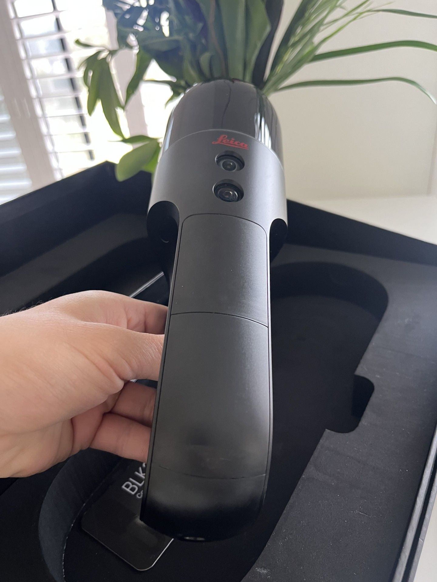 A person is holding a black device that says leica on it