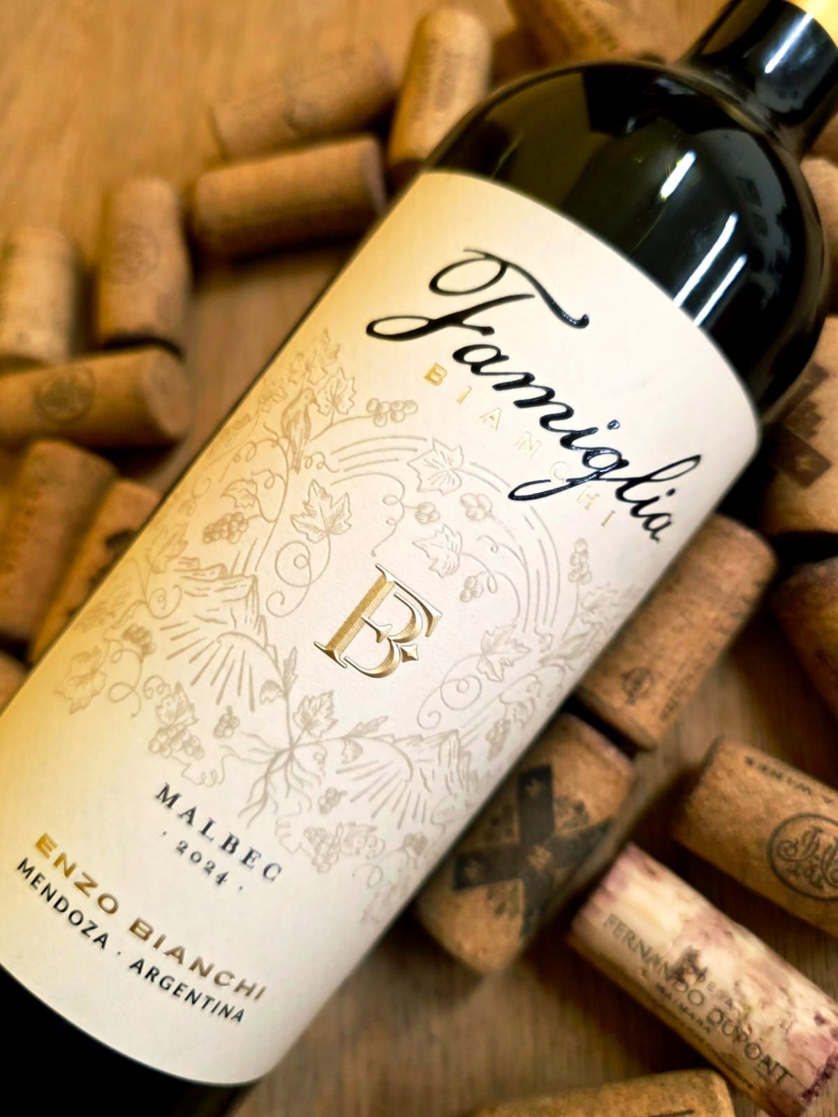 Una botella de vino Famiglia Bianchi Malbec sobre una mesa rodeada de corchos de vino esparcidos.