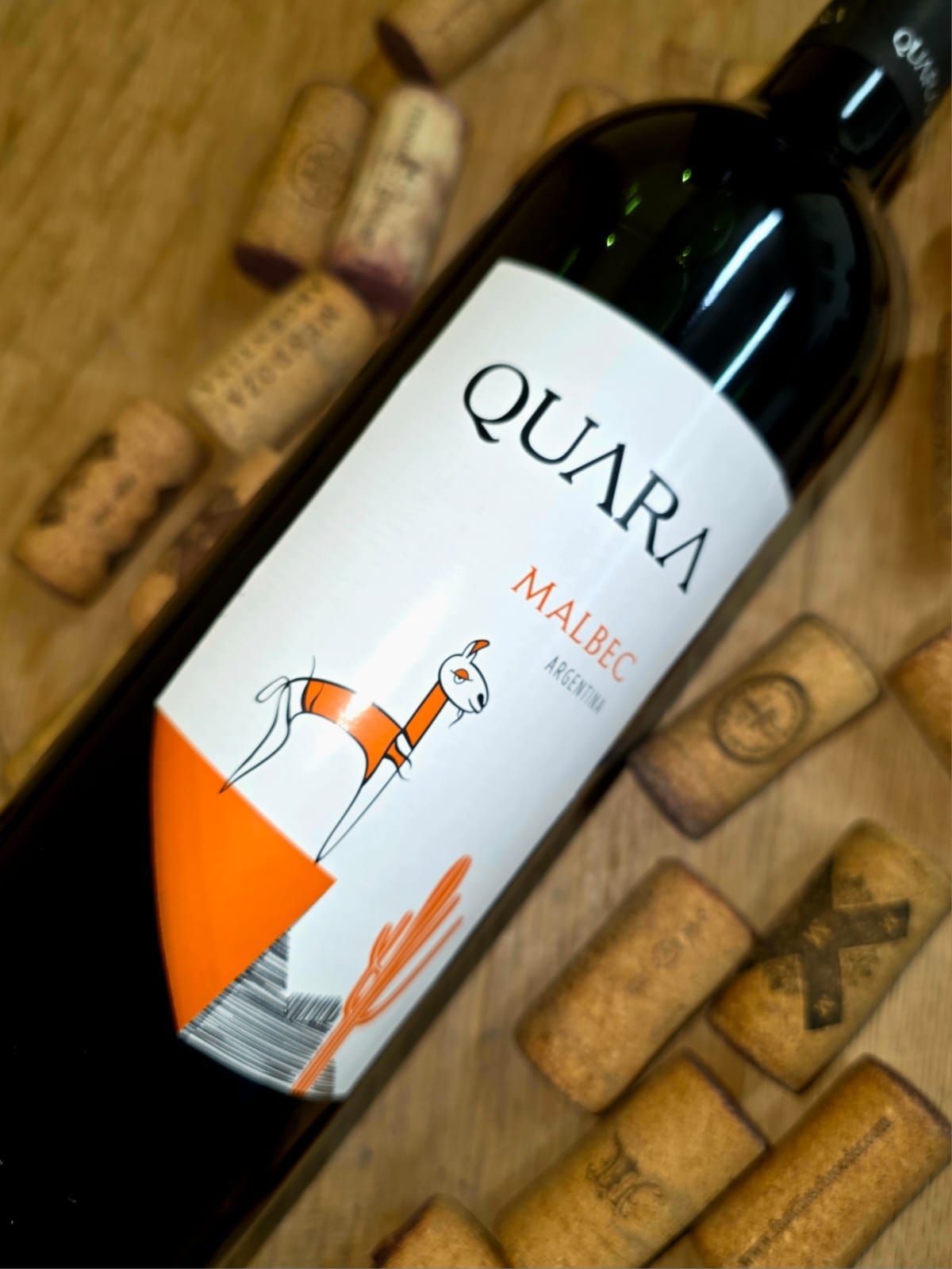 Una botella de vino Quara Malbec, con un gráfico de llama en su etiqueta, sobre una superficie cubierta de corchos de vino.