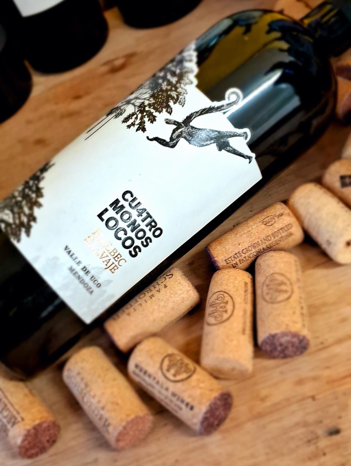 Una botella de vino Cuatro Monos Locos sobre una superficie de madera, rodeada de varios corchos de vino.