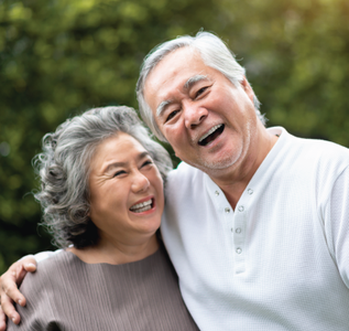 Smiling couple embracing outdoors. Woman in brown, man in white, both with gray hair.