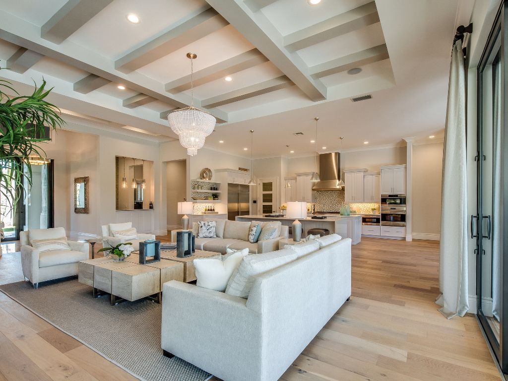 Spacious living room with light-colored furnishings, wood floors, and exposed ceiling beams; open to a kitchen.