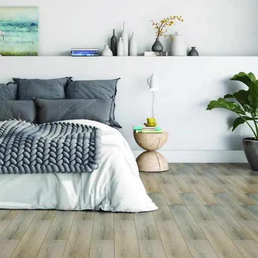 A bedroom with a bed , nightstand , plant and a painting on the wall.