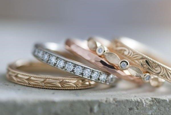 Four wedding rings of different designs stacked on a textured surface.