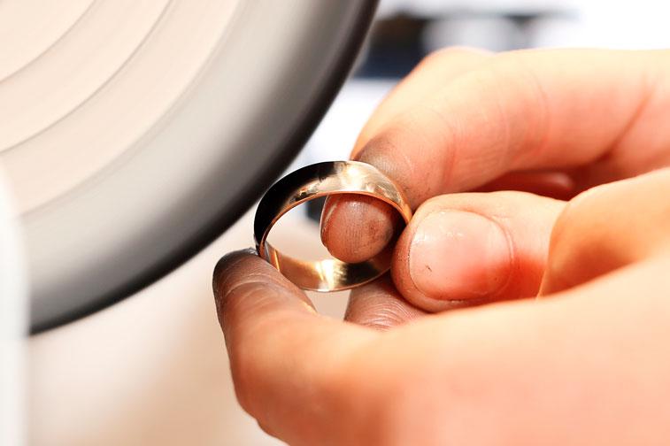 Hand holding a gold ring being polished with a buffing wheel, indoors.