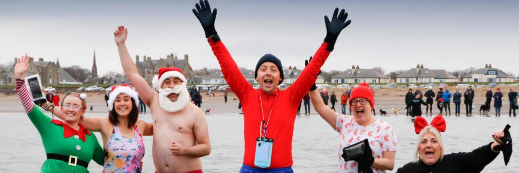 A group of people are standing in the water with their arms in the air at the Ayrshire Cancer Support annual Big Dip event