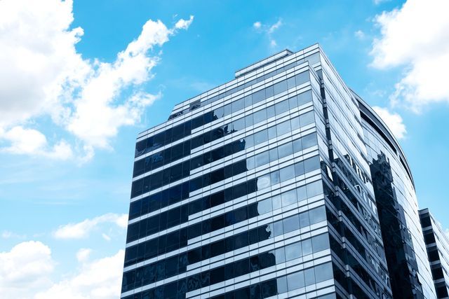 Modern glass skyscraper against a bright blue sky with fluffy white clouds.