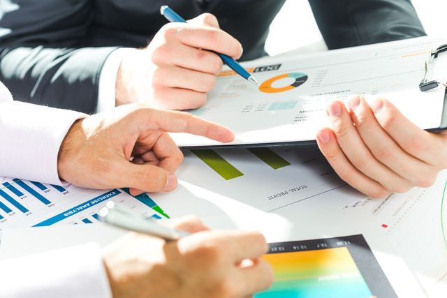 Business people reviewing financial reports with charts and a tablet. One person points to a chart.