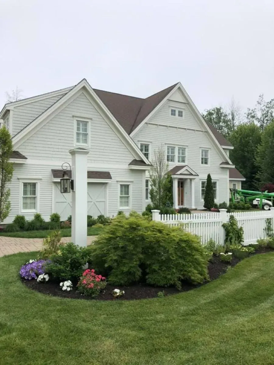 A large white house with a brown roof is surrounded by a lush green lawn.