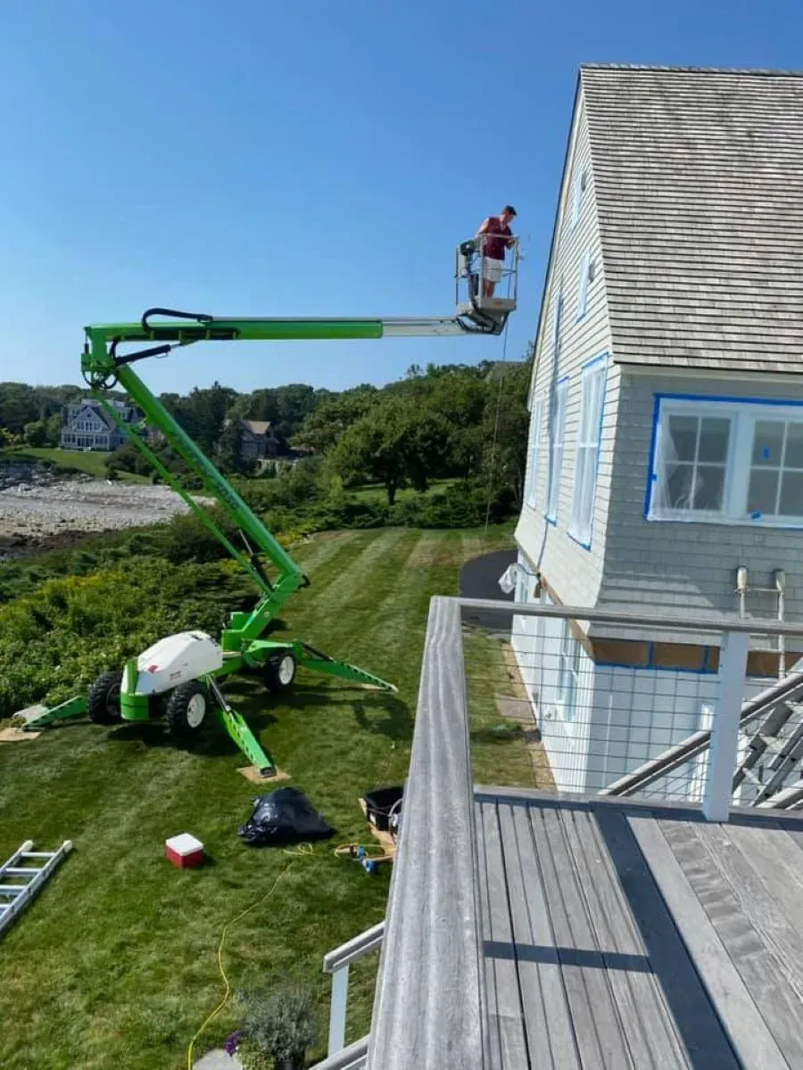 A man is painting the side of a house with a crane.