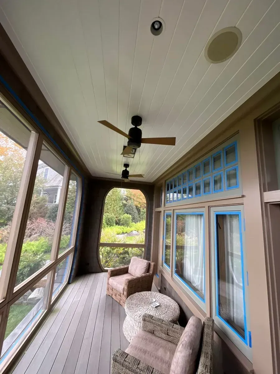 Covered porch with wood ceiling, ceiling fan, cushioned chairs, and blue-trimmed windows.