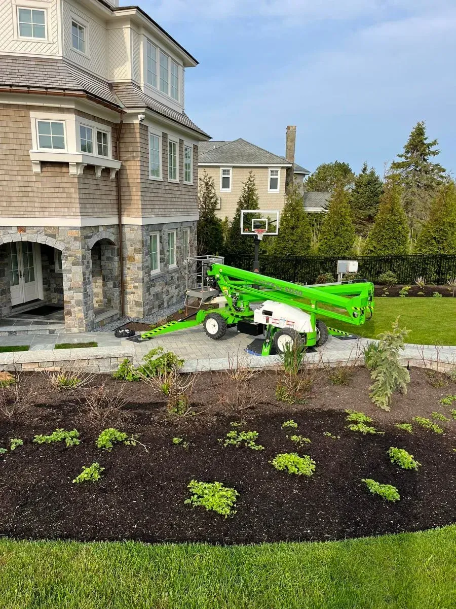 A green crane is parked in front of a large house.
