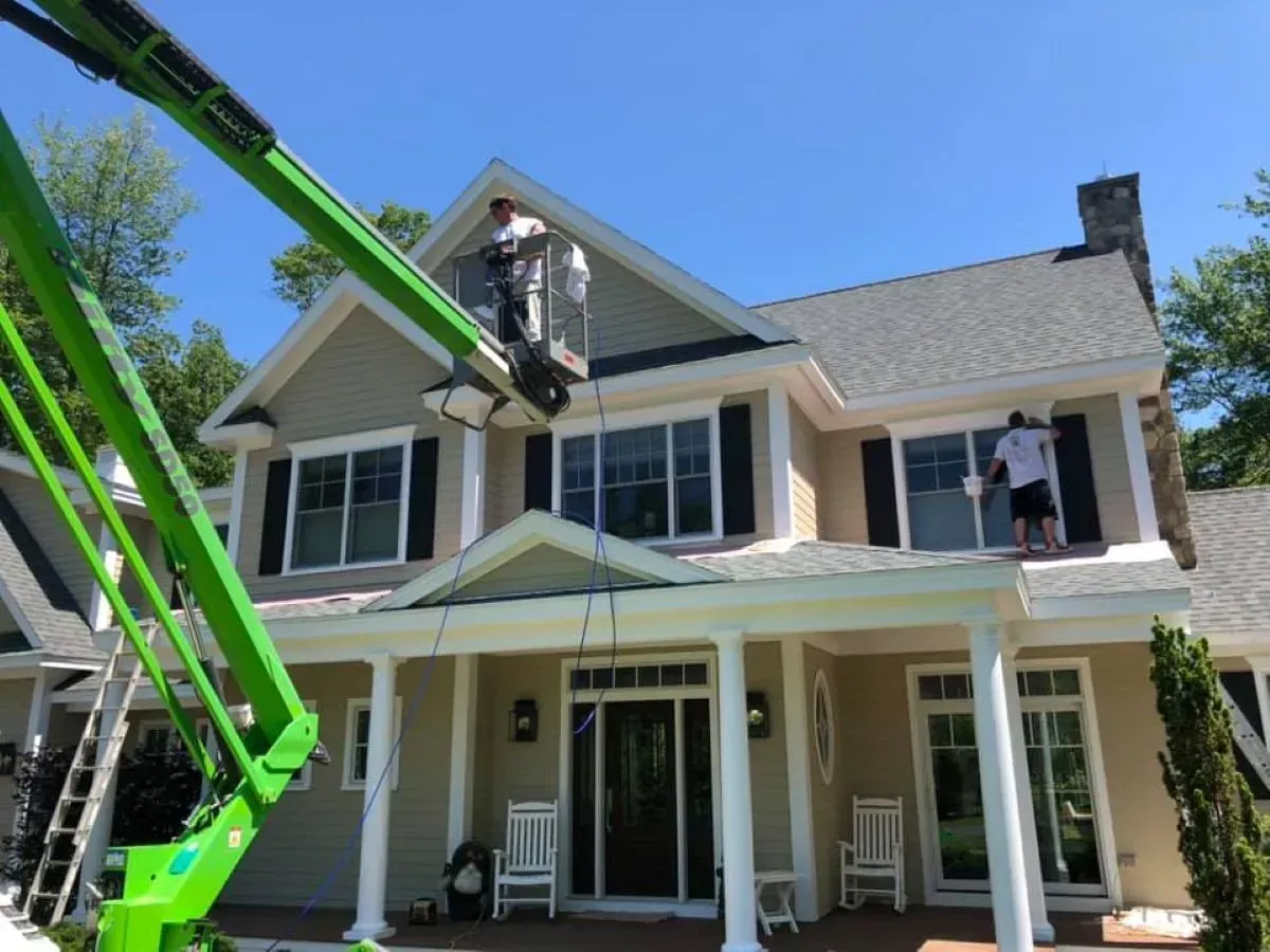 A man is painting the roof of a house with a green crane