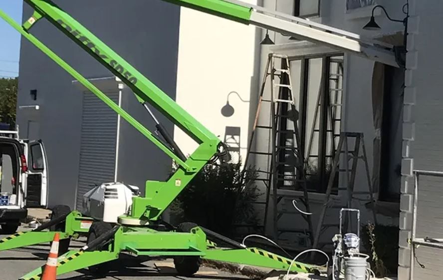 A green crane is parked in front of a building