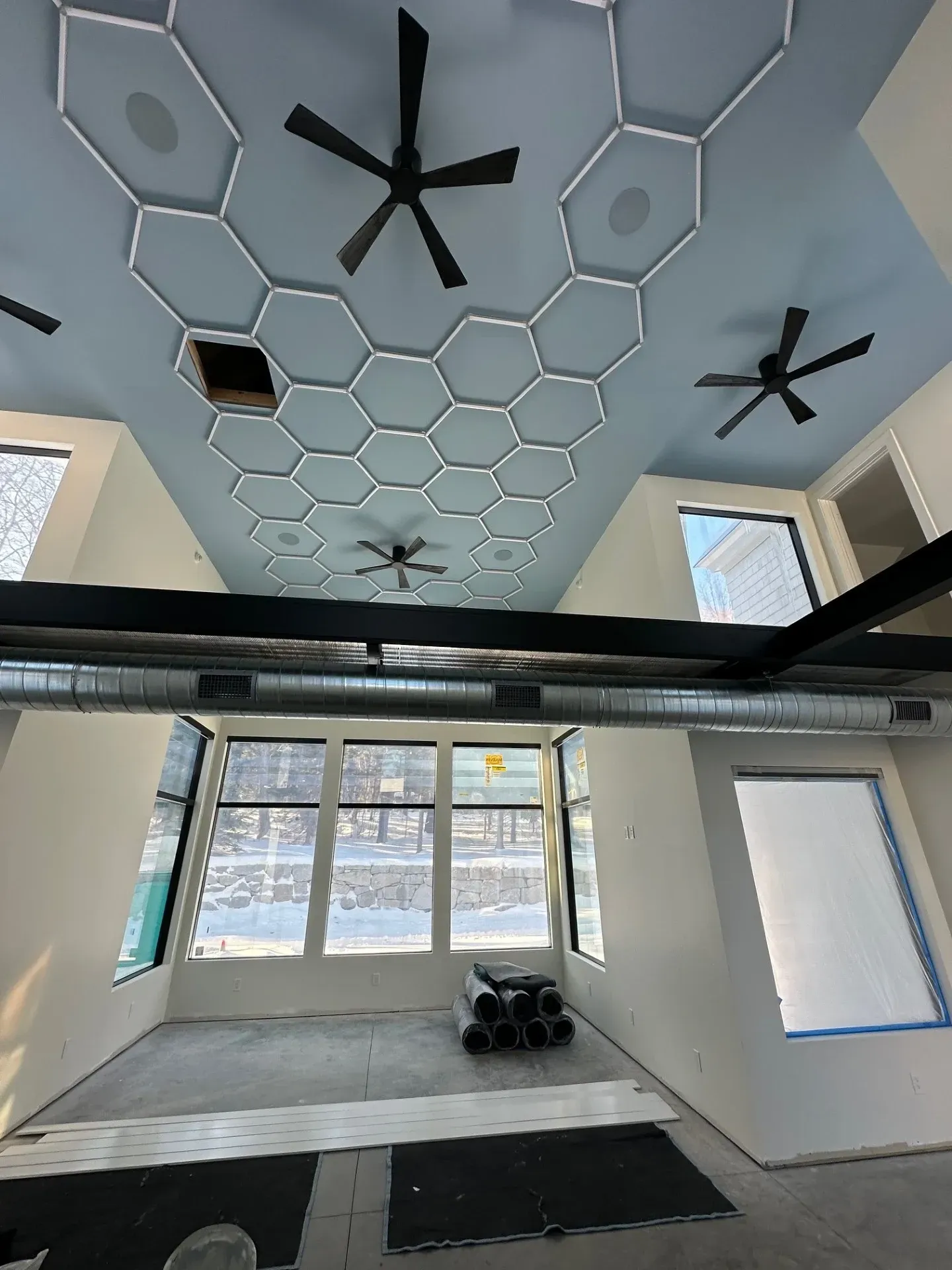 Modern loft interior with hexagon ceiling lights, black fans, and large windows overlooking snow.