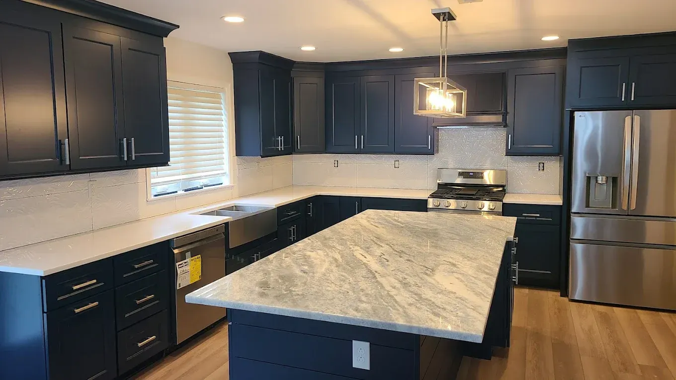 Kitchen renovation in progress with white upper cabinets, black lower cabinets, and unfinished walls and countertops.
