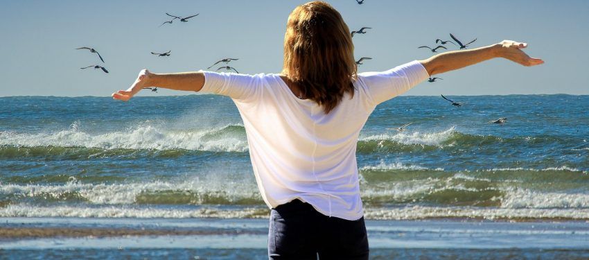 Person standing on a beach with arms outstretched facing the ocean