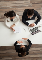 Three people in a meeting around a white table, with a laptop and papers in a bright office.