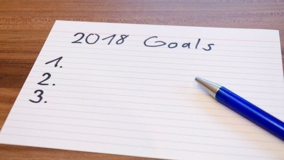 Handwritten “2018 Goals” on lined paper with a blue pen beside it and a numbered list.