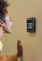 Person using a wall-mounted touchscreen device indoors, viewed in profile.