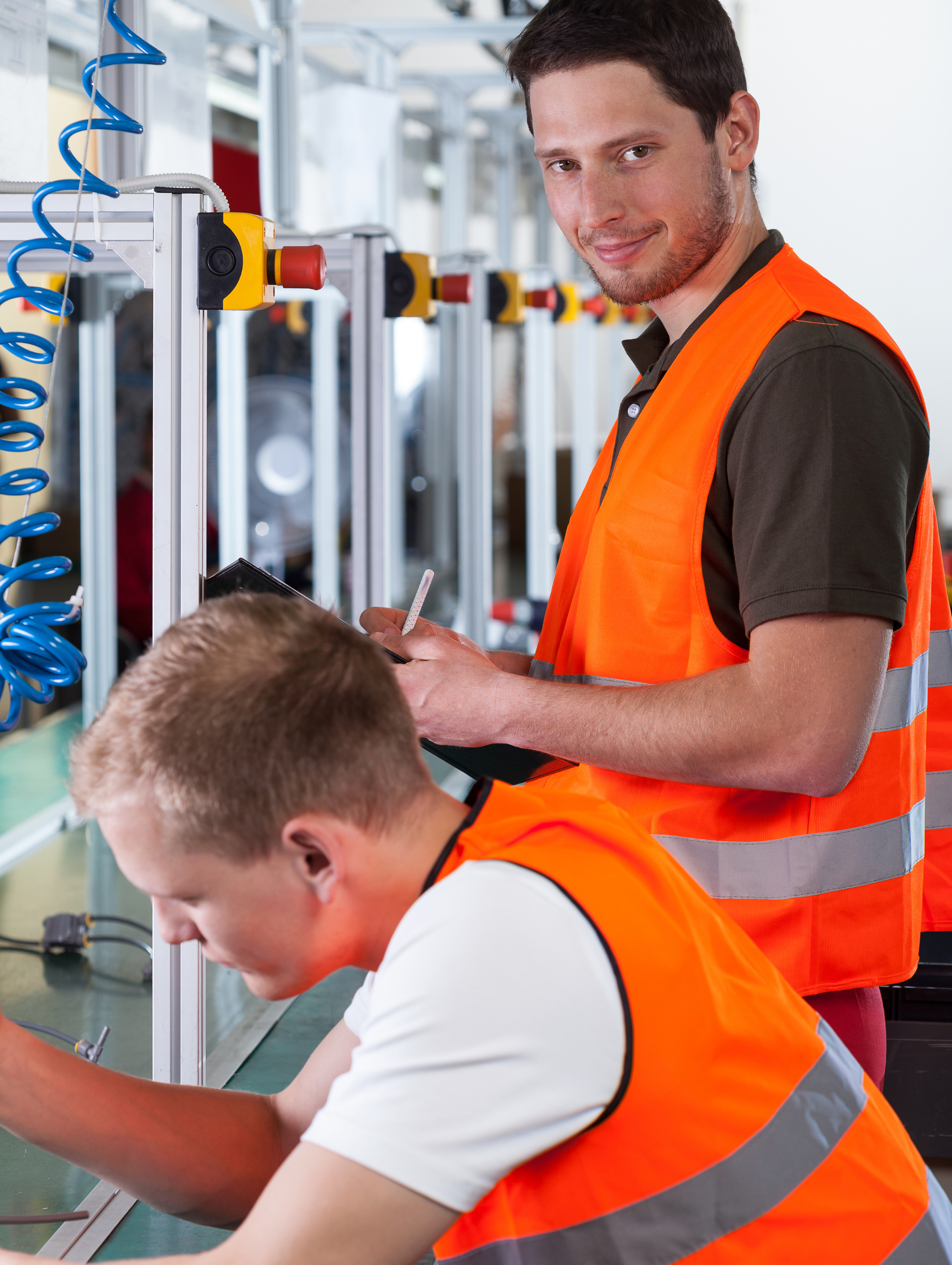 Two workers in orange safety vests operating industrial machinery in a workshop